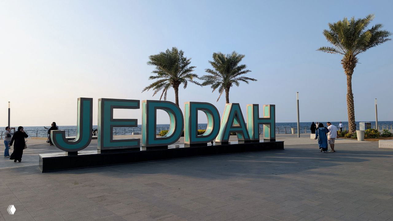 Набережная Джидды с большими буквами JEDDAH, пальмами и видом на Красное море — прибрежная прогулочная зона с прохожими.