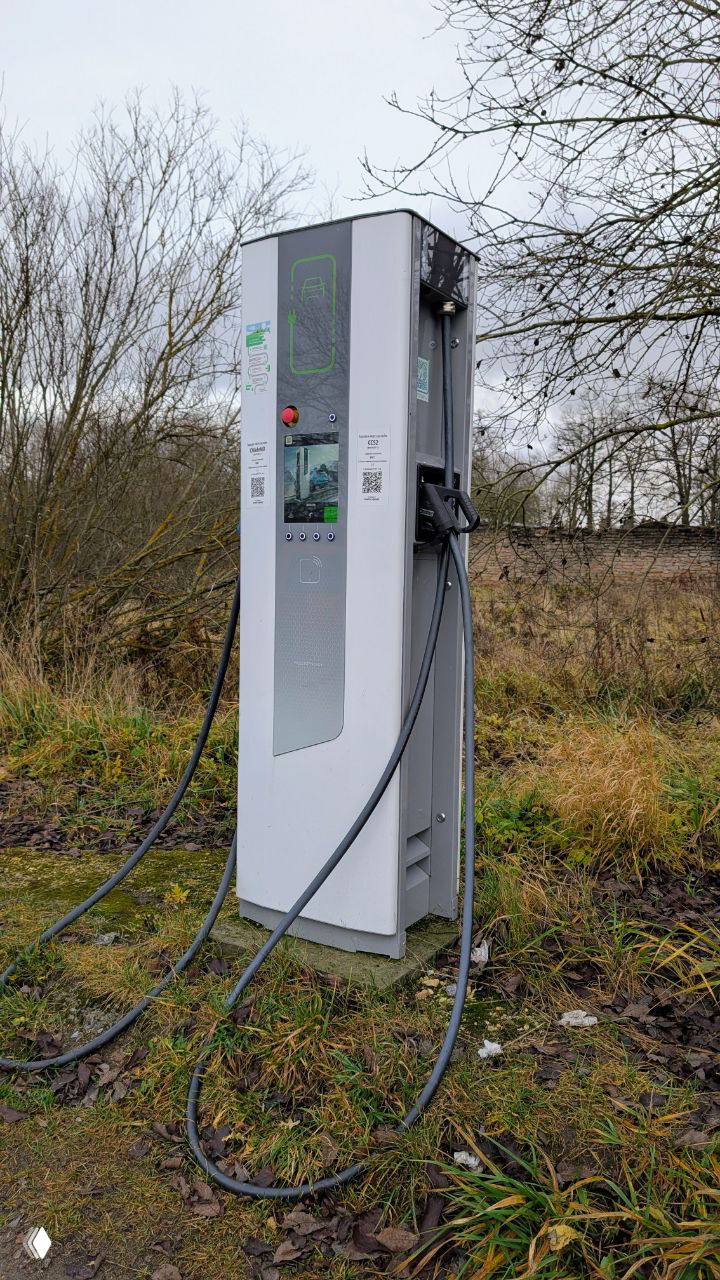 Колонка зарядки для электромобилей на земле у въезда в усадьбу Тайцы — контраст современной техники и заброшенного парка.