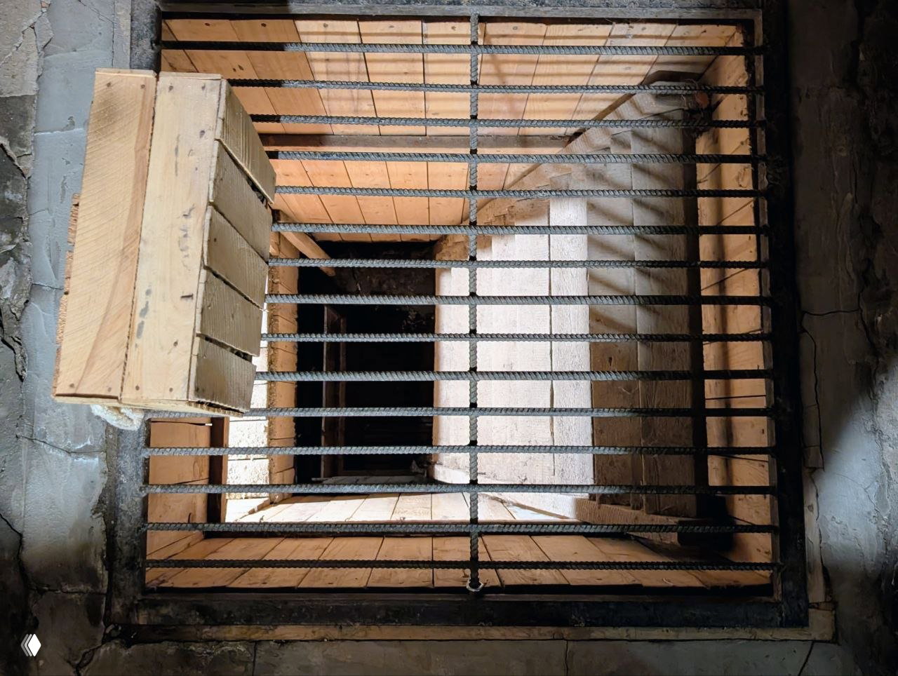 Вертикальный вид колодца/шахты с металлической решёткой и деревянной обшивкой — конструкция, прикрывающая вход к подпольному помещению.