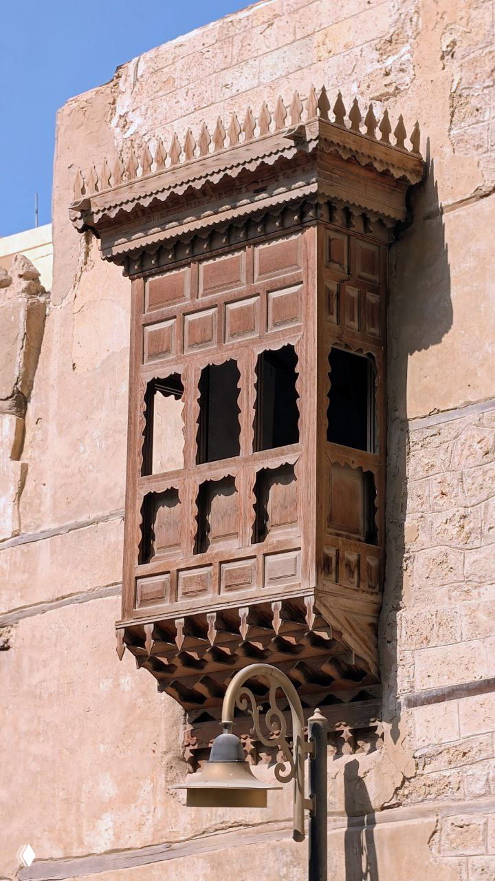 Деталь традиционной арабской архитектуры: вычурный деревянный эркер (машрабия) с резными элементами на фасаде старого дома, снято при дневном свете.