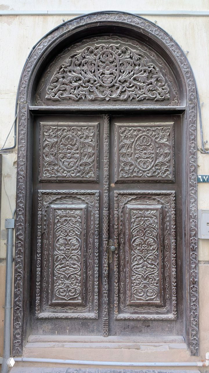 Архитектурная деталь: резные деревянные двери с арочным навершием и сложным растительным орнаментом — пример традиционной резьбы и оформления входов в старых кварталах.