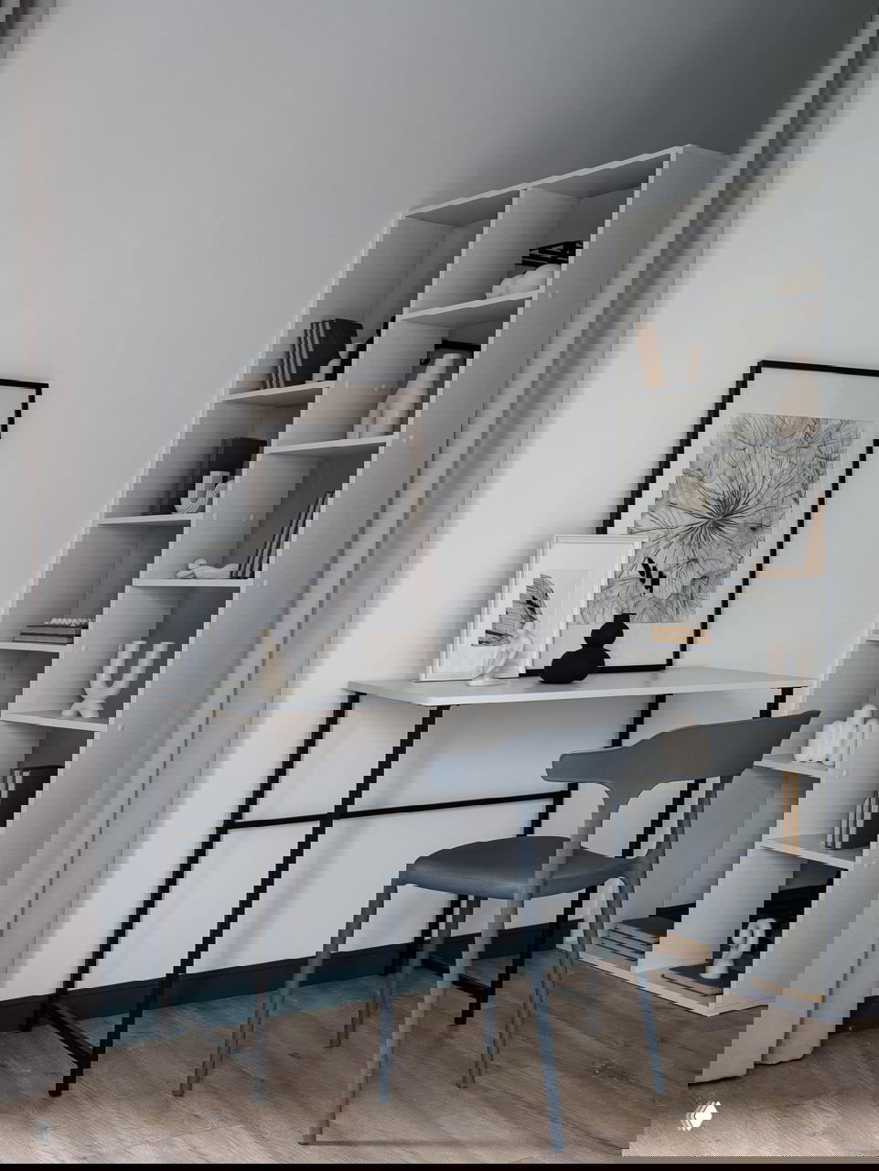 Рабочая зона у окна: минималистичный стол и стул на фоне высоких стеллажей и светлых стен, акцентная тёмно‑бирюзовая планка по периметру помещения.