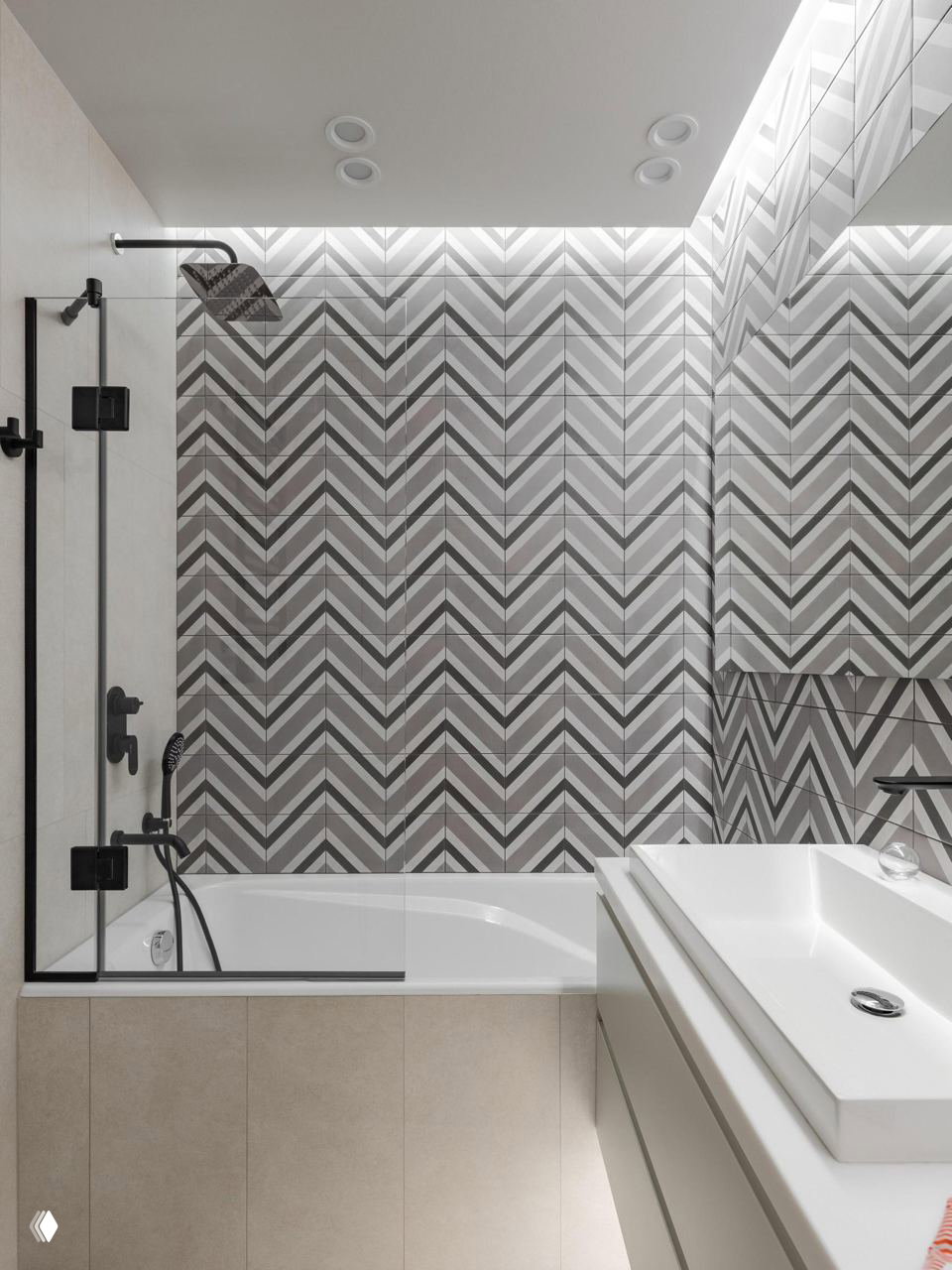 Ванная комната с ванной, современным черным душевым гарнитуром и графичными зигзагообразными серо-белыми настенными плитками в дизайнерском решении.