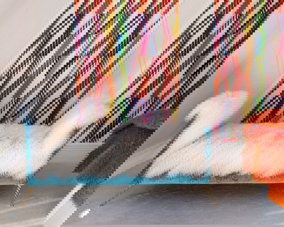 Яркая акцентная стена с геометрическим принтом за пушистым диванчиком — пример использования декоративных обоев для маскировки неровностей и создания фокальной зоны.