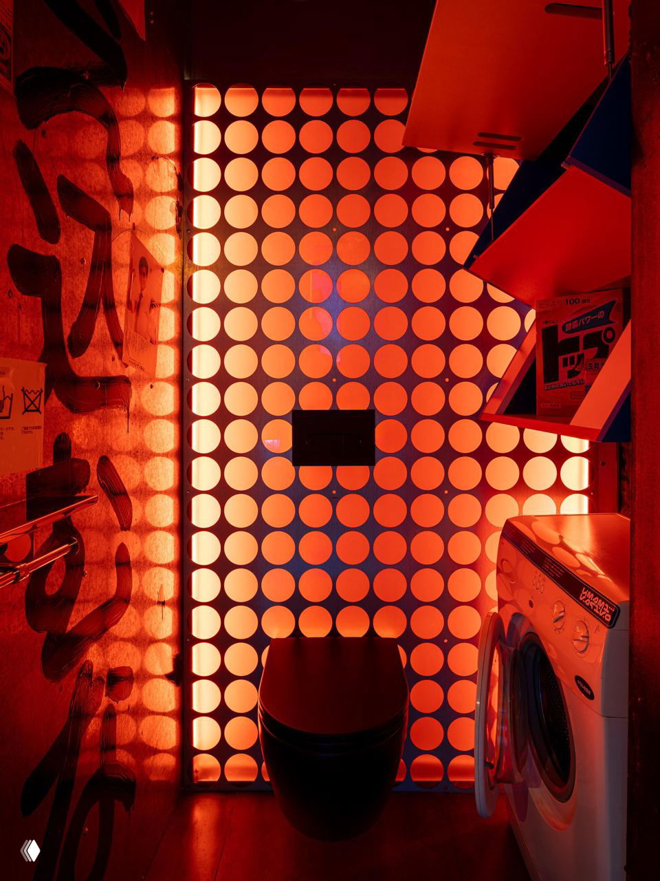 Туалетное пространство с перфорированной стеной, теплой красной подсветкой, висящим унитазом и стиральной машиной, оформленное в индустриальном стиле.