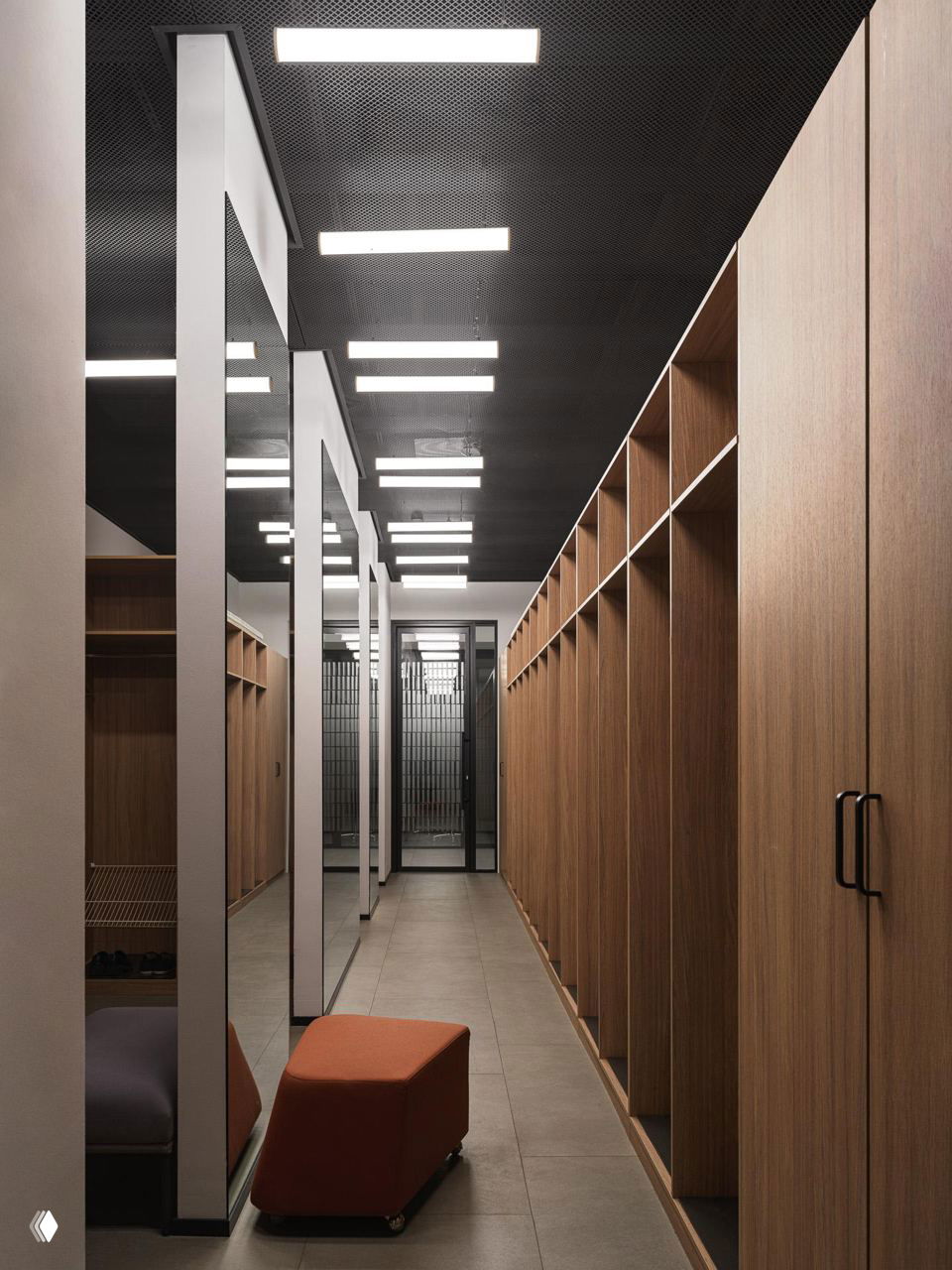 Гардеробная зона с длинными деревянными шкафчиками, зеркалами, узким проходом и мягким пуфом на колесиках — практическое решение в офисе 2ГИС в Москве.