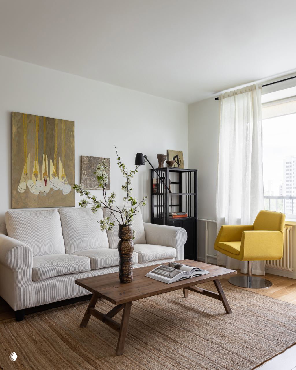 Гостиная зона: светлый диван с текстурной обивкой, низкий деревянный журнальный стол, яркое жёлтое кресло и декоративные работы на стене над диваном.