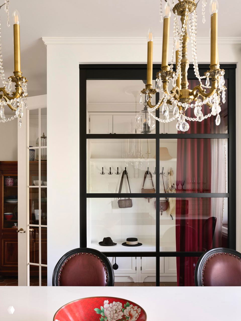 Столовая с чёрной стёклянной перегородкой, золотой хрустальной люстрой, красной вазой на переднем плане и кинематографичной атмосферой.