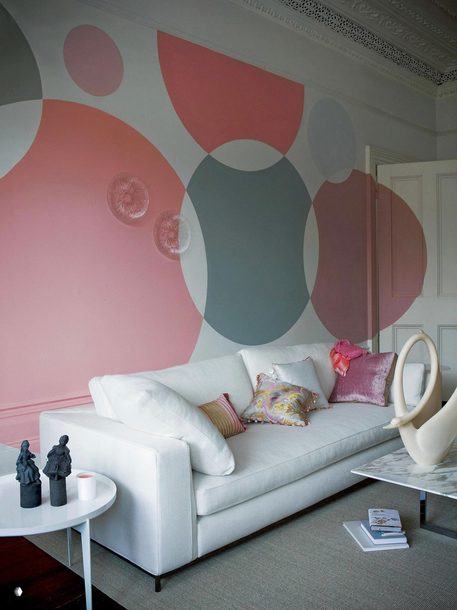 Гостиная с декоративным принтом из больших округлых форм на стене в пастельных тонах, светлый диван и текстиль создают мягкую атмосферу.