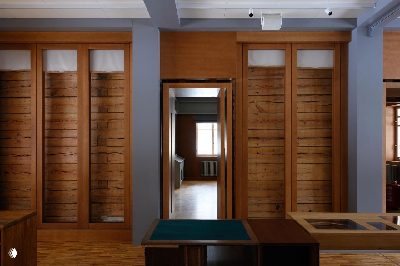 Внутреннее пространство музея: выставочная зона с паркетным полом, деревянными стеновыми панелями и проходом к окну, строгая экспозиция.