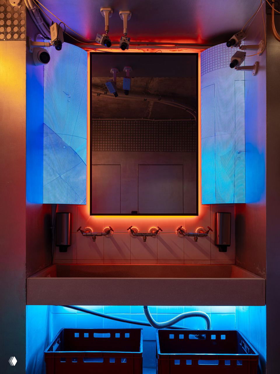 Раковина и большое зеркало в туалете кафе с RGB‑подсветкой, экранными панелями по бокам и неоновыми акцентами в кибер‑стиле.