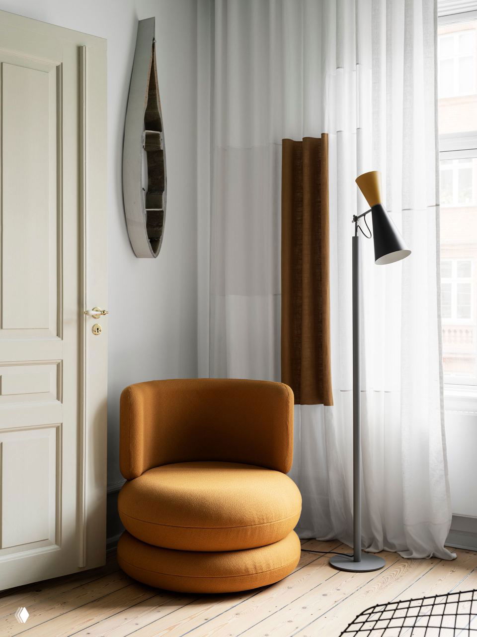 Уютное круглое кресло горчичного цвета у окна, рядом напольная лампа и тонкие занавеси — акцентный предмет в спокойной палитре скандинавского интерьера.