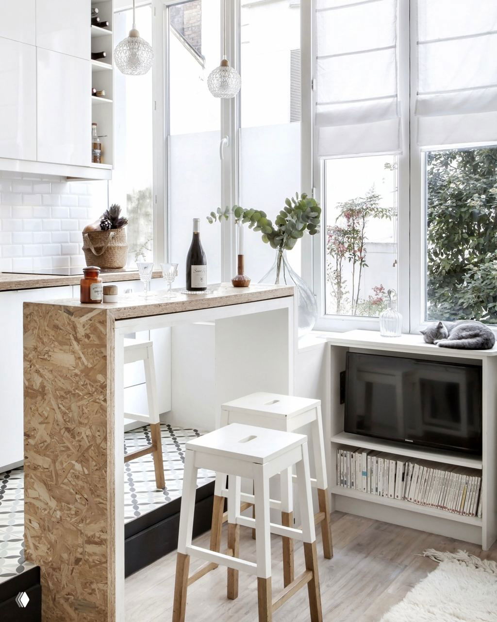 Светлая компактная кухня с барной стойкой из ориентировано-стружечной плиты (OSB), деревянные табуреты и большие окна; интерьер сочетает практичность и лёгкую небрежность.