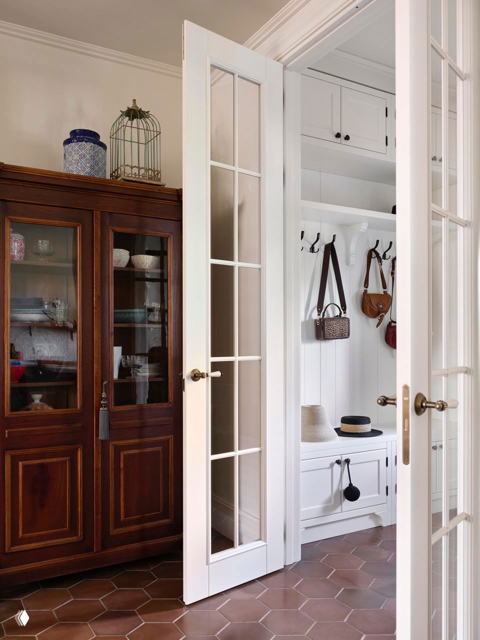 Прихожая с массивным деревянным буфетом, белой дверью со стеклами и вешалками с сумками — сочетание антиквариата и практичных решений.