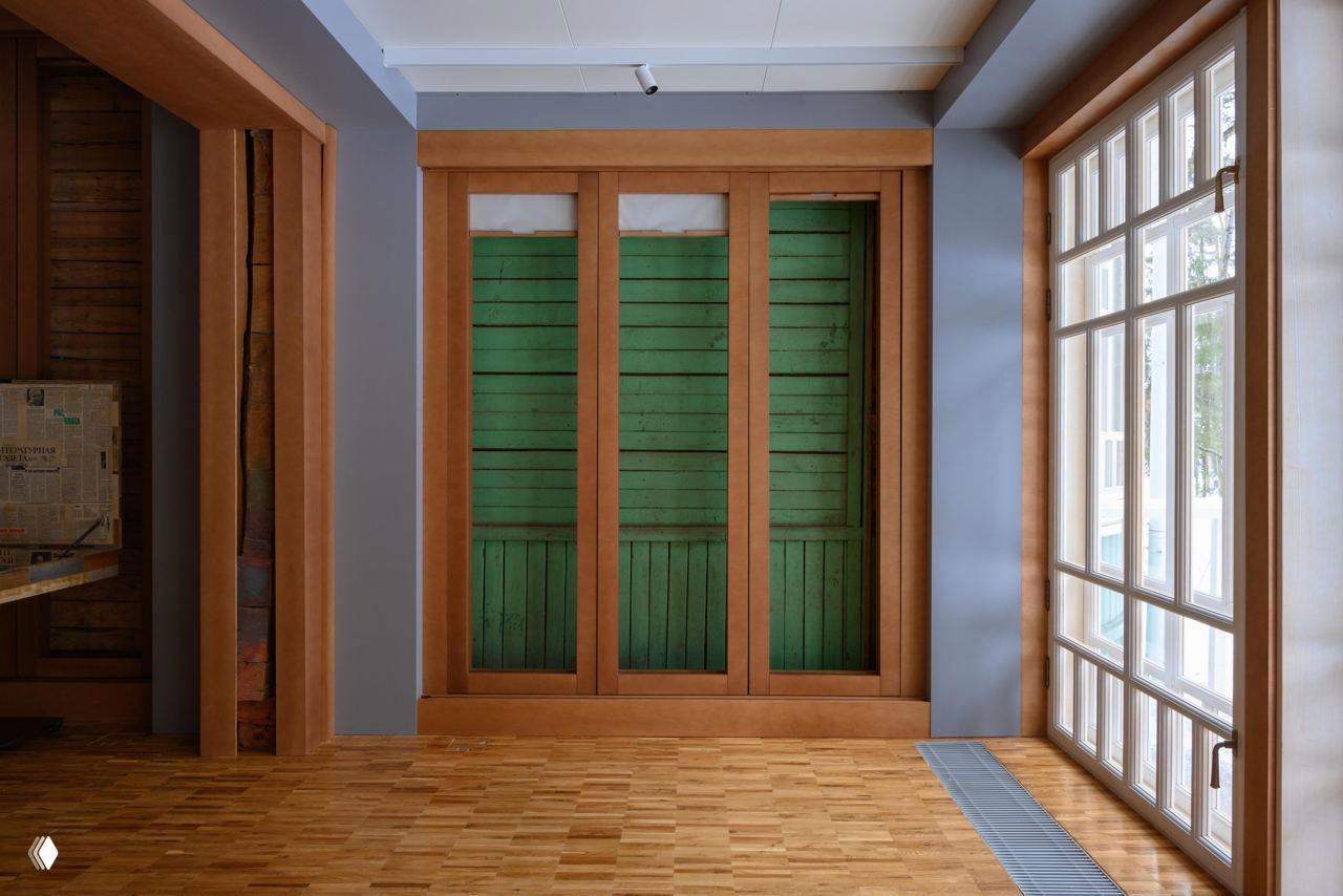 Интерьер 'Первой дачи': панно из старых зелёных досок за рамой, светлые окна в пол, деревянный паркет и атмосферное освещение.