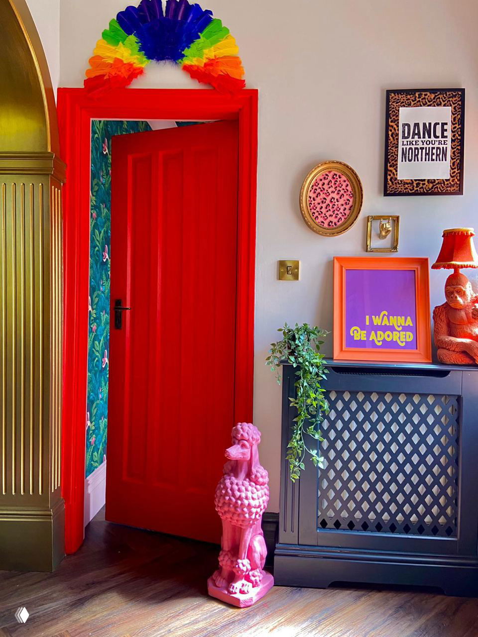 Эклектичный интерьер прихожей с ярко-красной дверью, цветными рамками, декоративной статуэткой и контрастными аксессуарами — пример смелого акцентирования входной зоны.