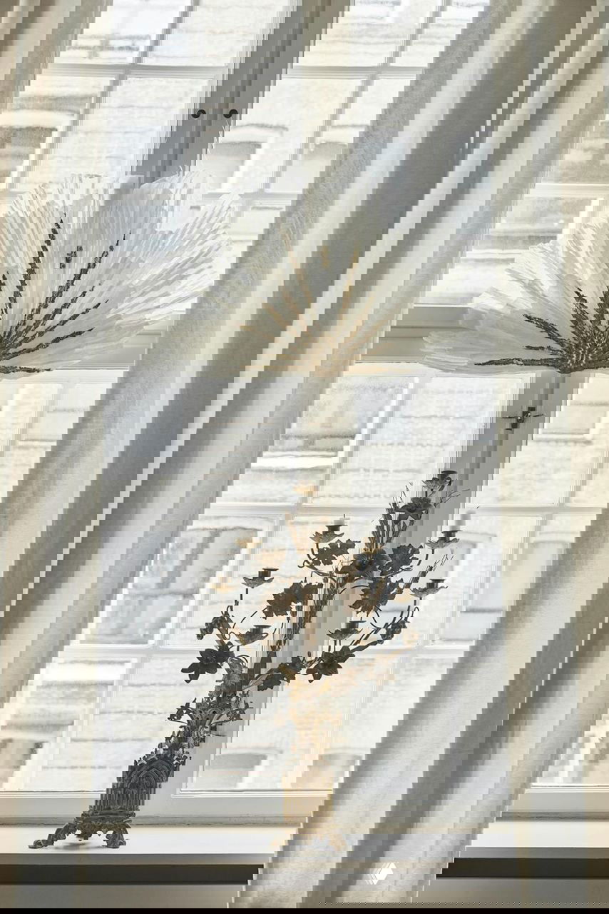 Угол гостиной с большим окном и белым диваном: ажурное бумажное украшение на стекле, рамка с картиной и мягкая естественная подсветка.