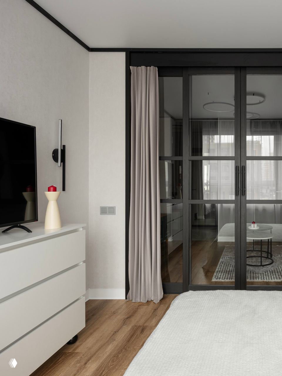 Вид на спальню с раздвижными тёмными створками и телевизионной зоной; мягкие шторы, светлая кровать и деревянный SPC-пол в интерьере.