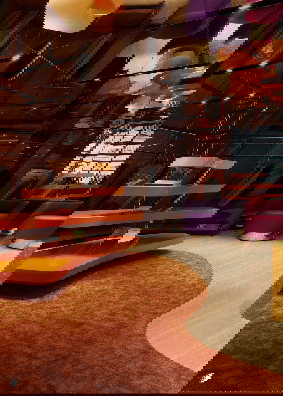 Панорамный вид торгового пространства: глянцевые витрины, низкие подиумы оранжевого цвета и пурпурные мягкие кресла в зоне примера.