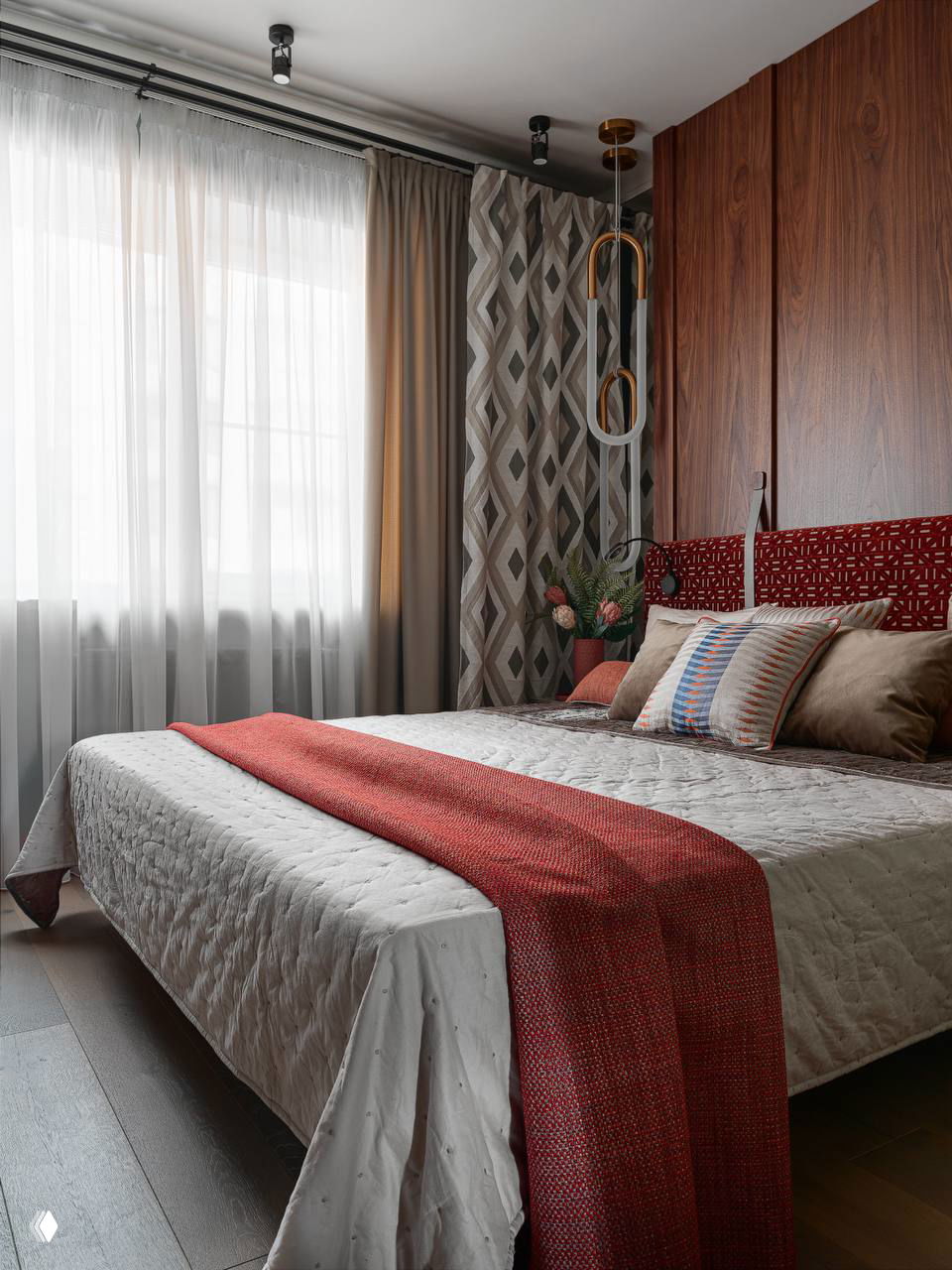 Спальня в нейтральных и коричневых тонах с декоративными геометрическими шторами, текстильными акцентами и красно‑терракотовым пледом для теплоты образа.