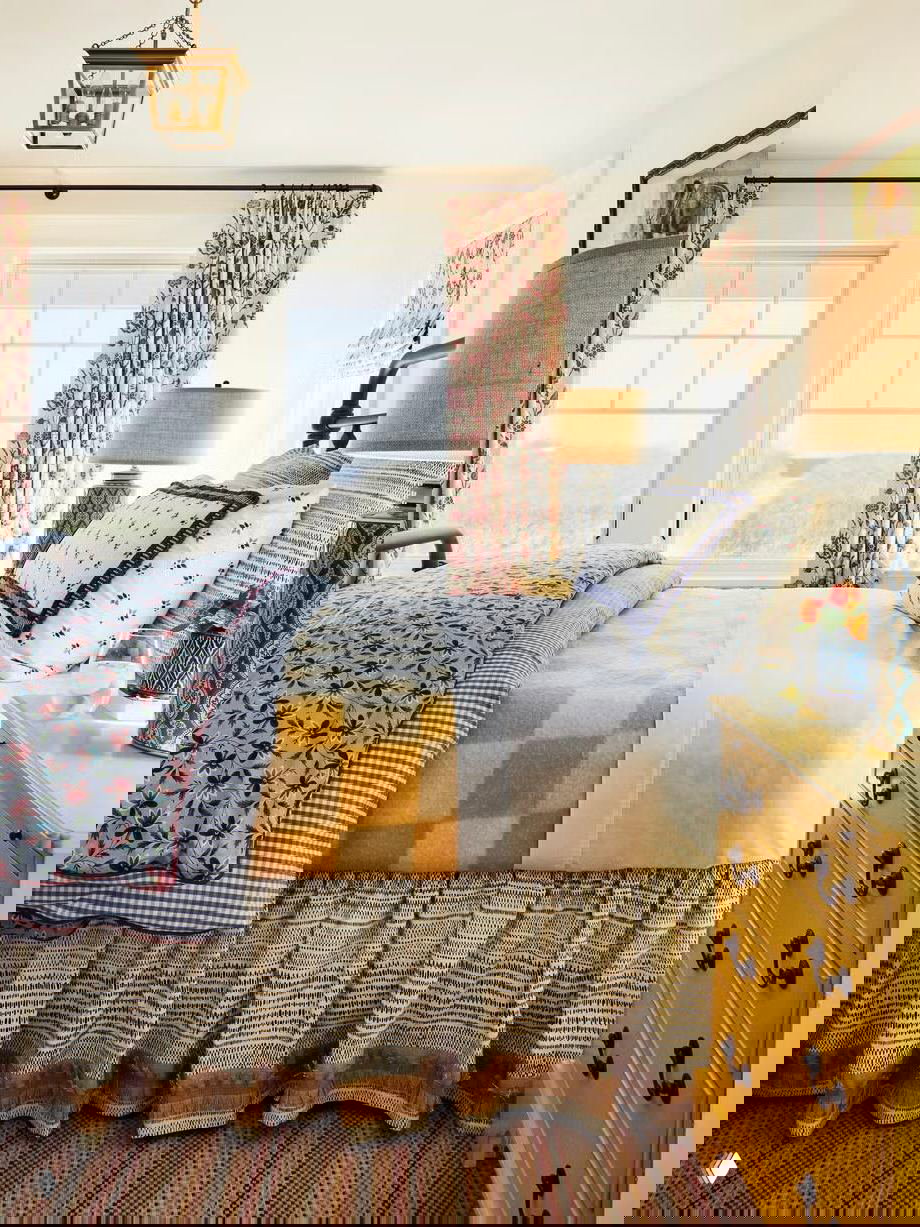 Прибрежная по настроению спальня с большим окном, пёстрым текстилем, жёлтым пледом и классическим комодом у окна — светлый уютный интерьер для гостей.