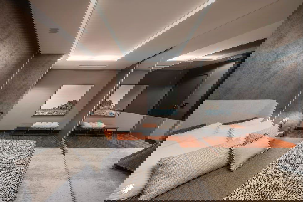 Спальня с низкой кроватью, тёплым деревянным настилом у изголовья и зеркальными дверями шкафа, спокойная нейтральная гамма и текстуры.