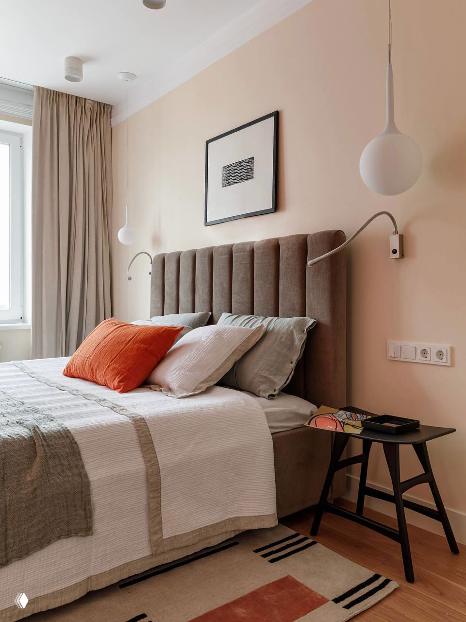 Пастельно‑коричневая спальня с мягким изголовьем, светлыми текстурами и контрастной терракотовой подушкой — спокойная и уютная атмосфера для сна.