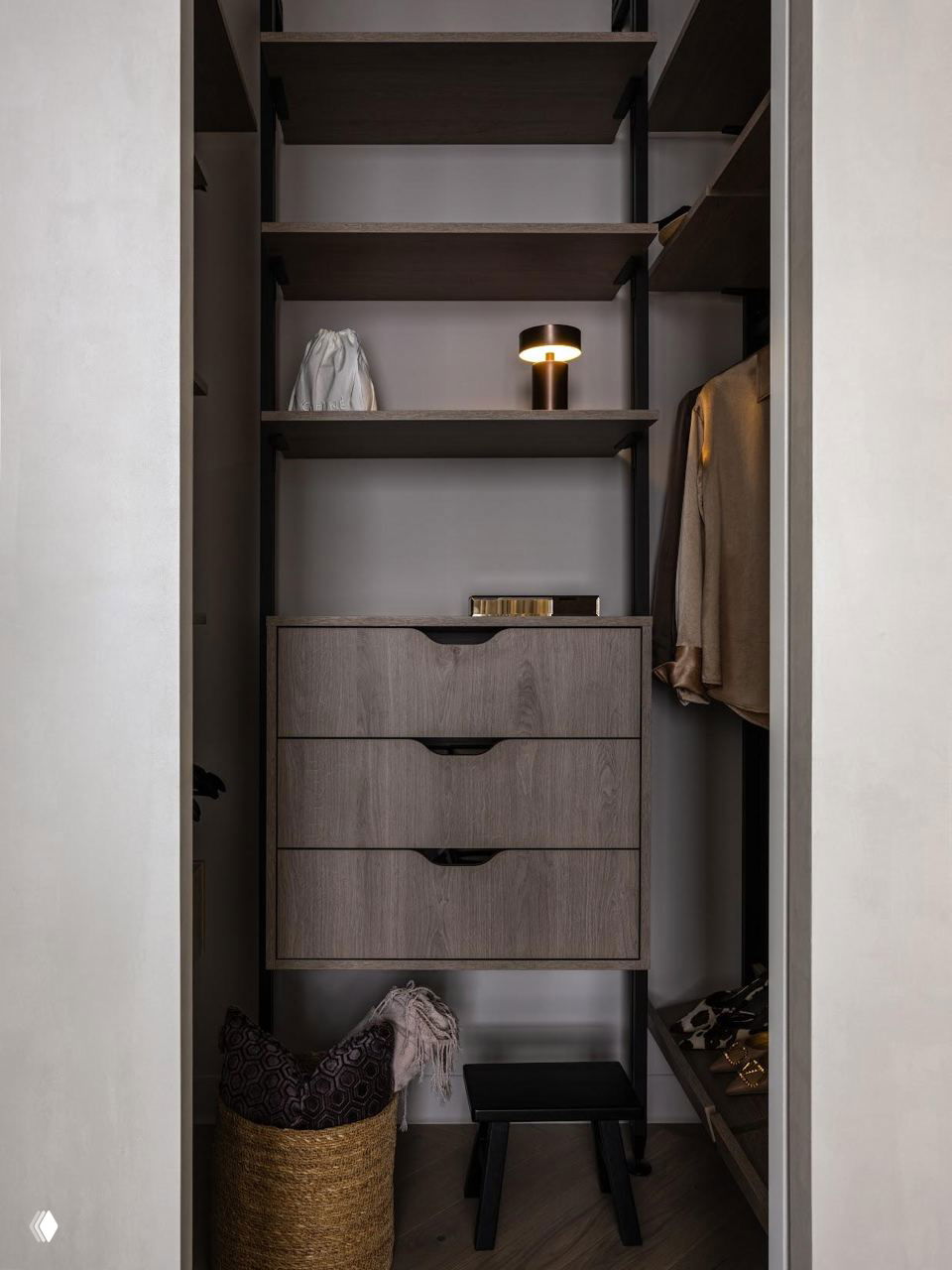 Ниша гардеробной с тёмными полками и ящиками, аккуратно развешенная одежда и корзина — компактное функциональное хранение в светлом минималистичном интерьере.