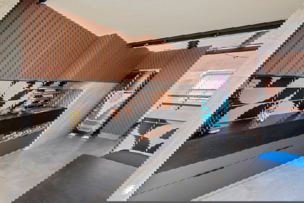 Кухня с чёрной столешницей, графичным фартуком в чёрно‑белую геометрию, навесными деревянными панелями и светлым каменным полом.