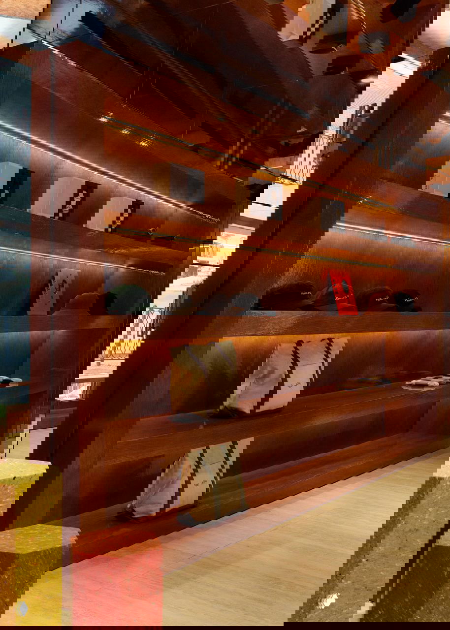 Деревянные полки и стеллажи из шпона ореха с подсветкой, на полках сумки и головные уборы в минималистичной выкладке.