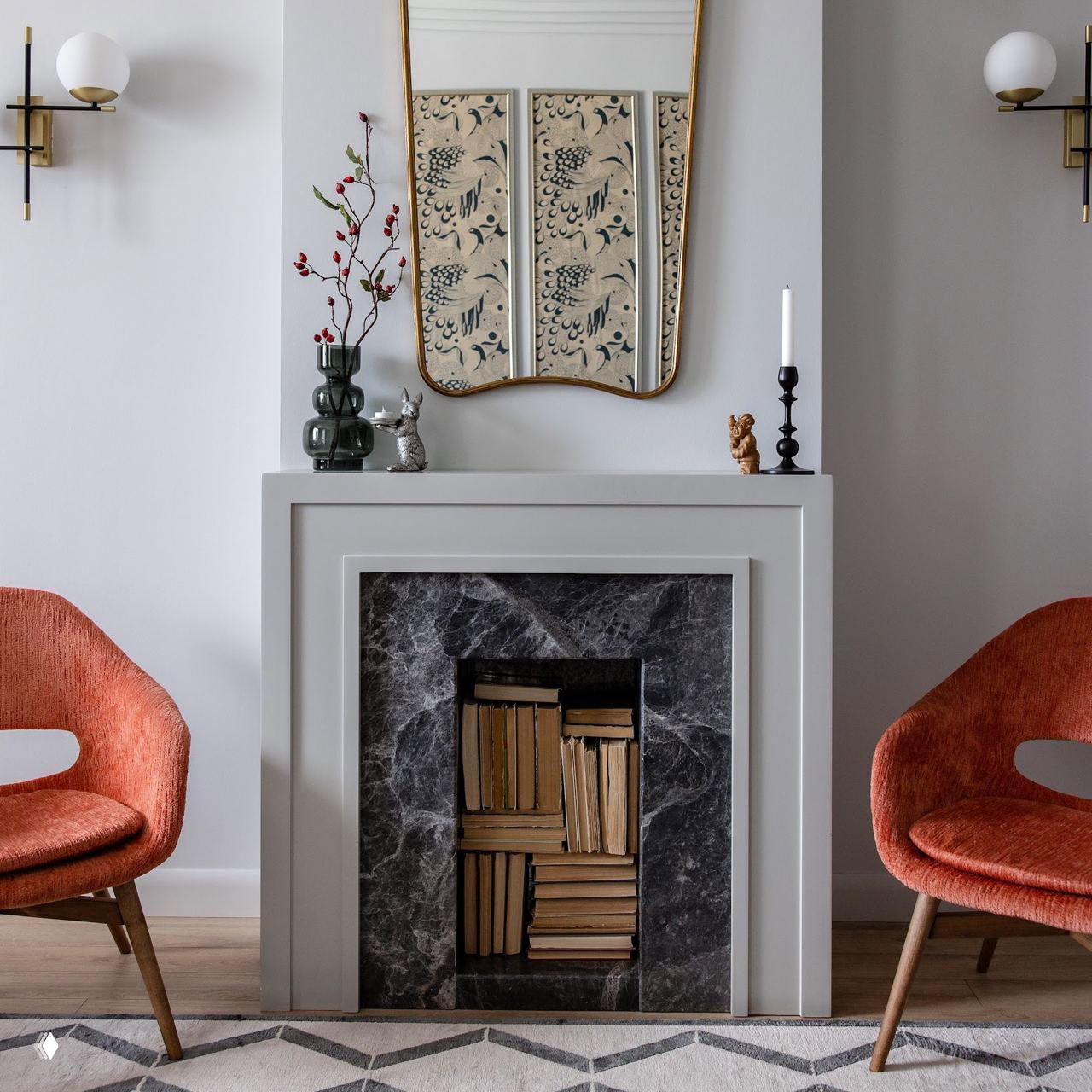 Минималистичная гостиная с декоративным камином, книгами внутри ниши и двумя небольшими бра — пример стильного оформления небольшого пространства с помощью света.