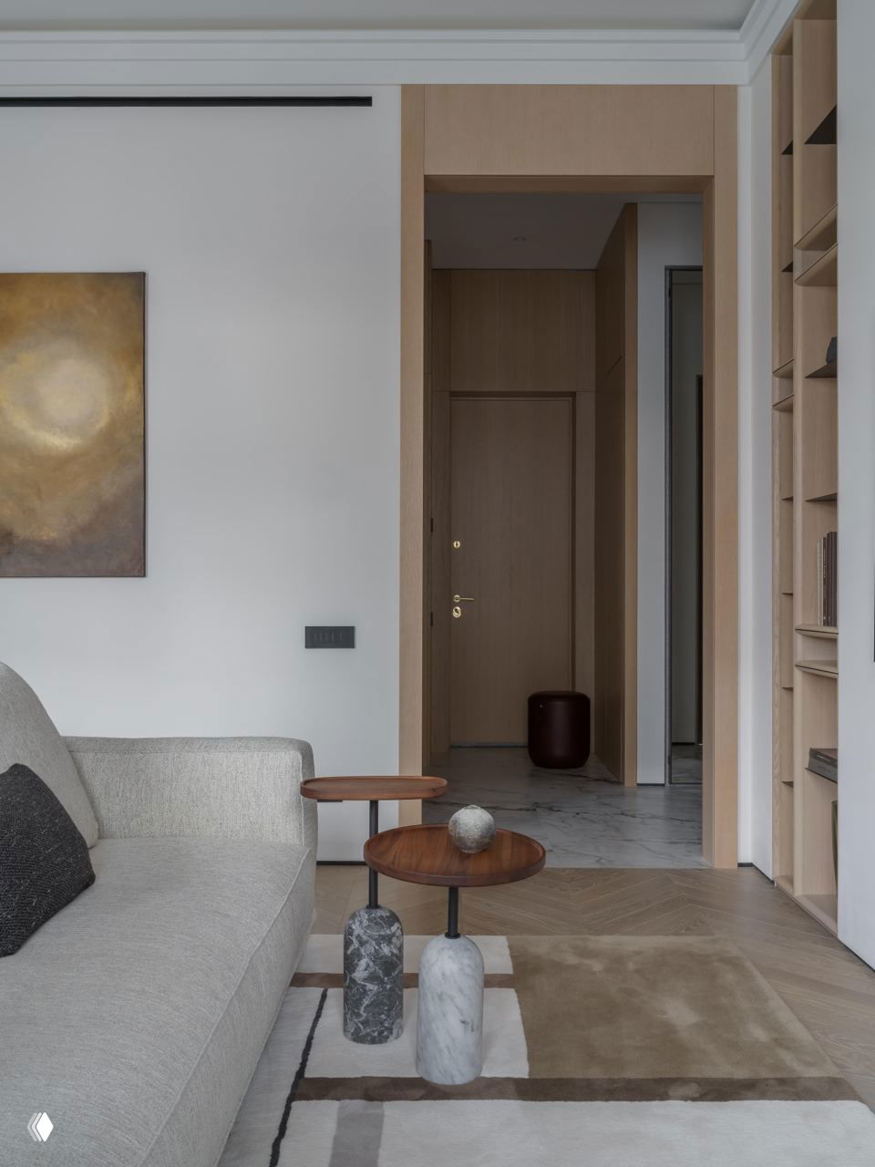 Угол гостиной с текстильным диваном и парой круглых приставных столиков на мраморных основаниях; вид в сторону входного коридора и деревянной отделки.