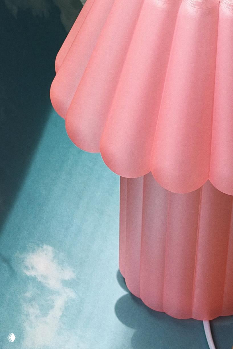 Крупный план верхней части розовой лампы Jello Lamp: мягкая ребристая структура абажура, матовая поверхность и видимый электрический шнур на голубом фоне.