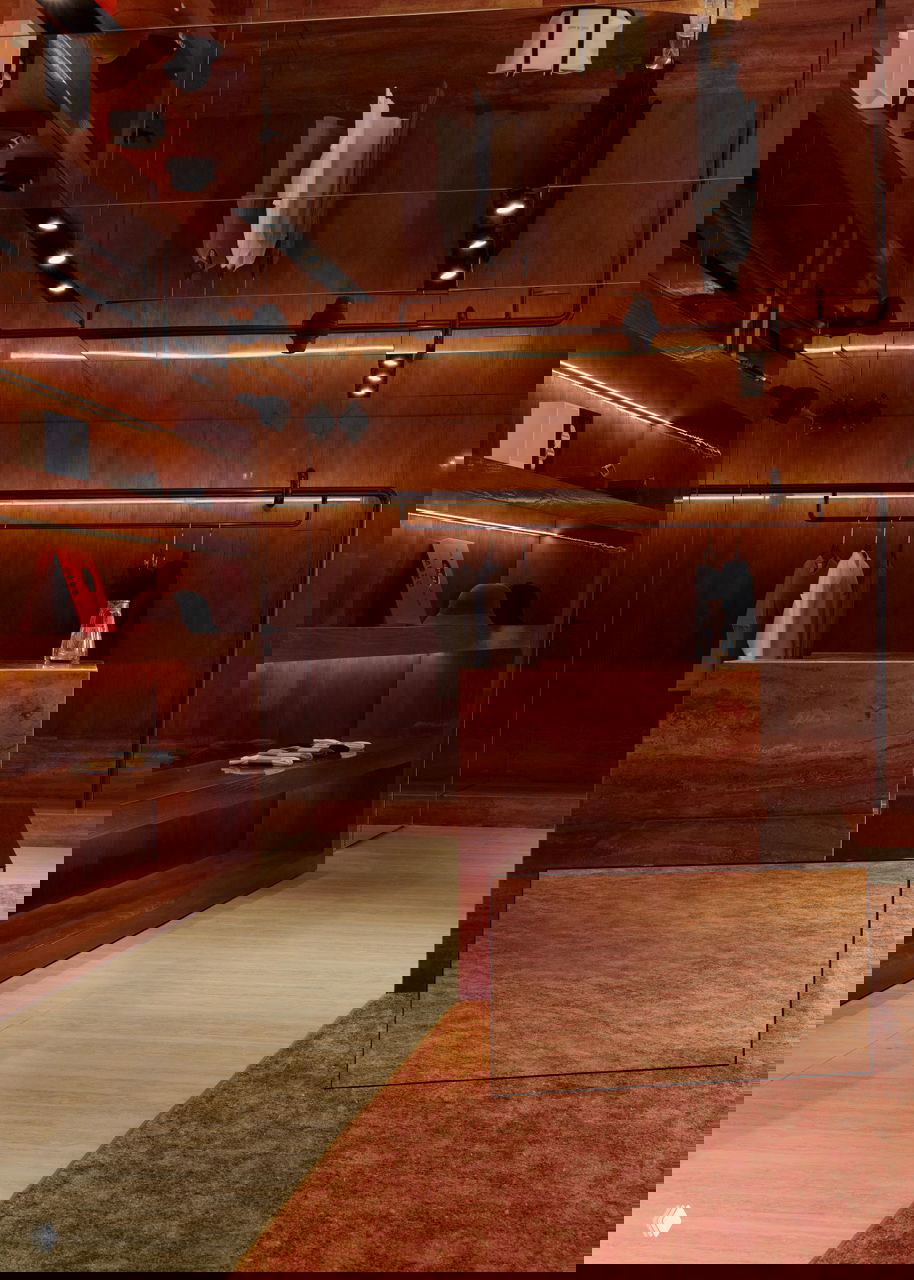 Композиция из блоков и подиумов с трауретиновыми вставками и зеркальными элементами на фоне тёплой деревянной отделки и ковра.