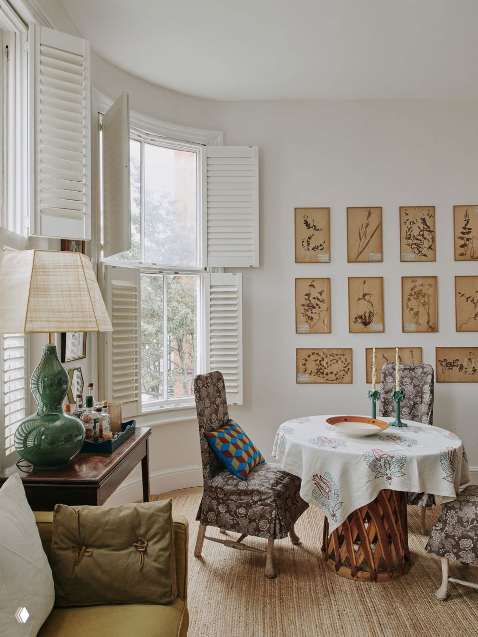 Столовая с круглым столом и обеденными креслами, на стене — серия старинных ботанических листов гербария в тонких рамках, ключевой акцент интерьера.