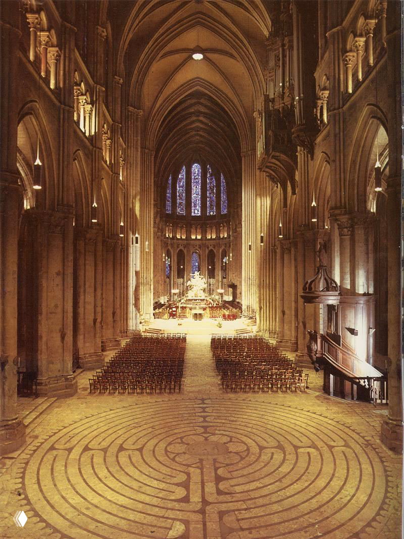 Интерьер готического собора с видом на неф, алтарь и центральный узор лабиринта на мраморном полу под мягким светом витражей.