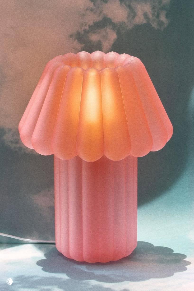 Jello Lamp освещена тёплым мягким светом: розовый матовый абажур излучает тёплое свечения, подчёркивая форму, похожую на желейный десерт, на небе фоне.