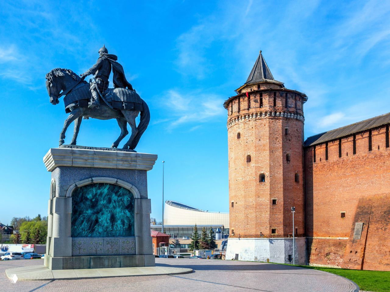 Памятник всаднику и одна из круглых башен Коломенского кремля на фоне синего неба, открытое пространство исторического центра.