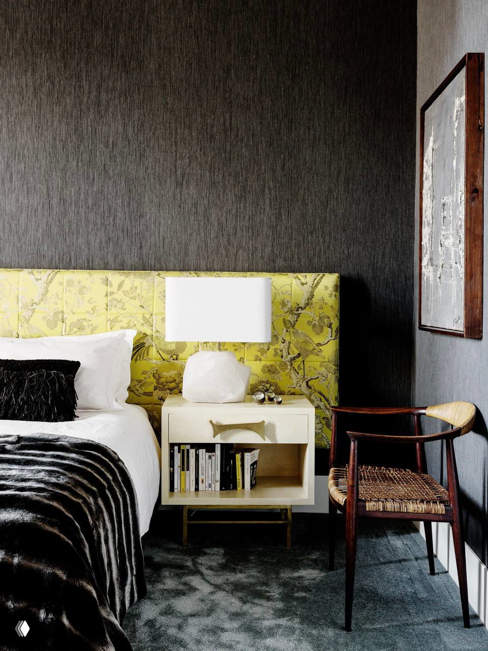 Стильная спальня с темной акцентной стеной и ярким текстильным изголовьем салатового оттенка, тумбочка со стеклянной лампой и журнальный столик рядом.