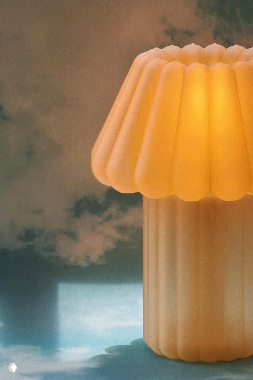 Фрагмент светящейся лампы Jello Lamp: тёплое свечение просвечивает через рифлёный абажур, создавая мягкие тени и пастельные оттенки на фоне небесного принта.