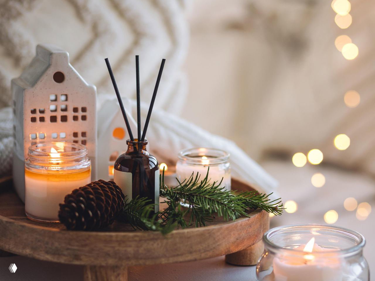 Маленький стеклянный флакон‑диффузор на деревянной подставке среди горящих свечей, шишки и еловая веточка — рождественская, уютная интерьерная сцена в студийном освещении.