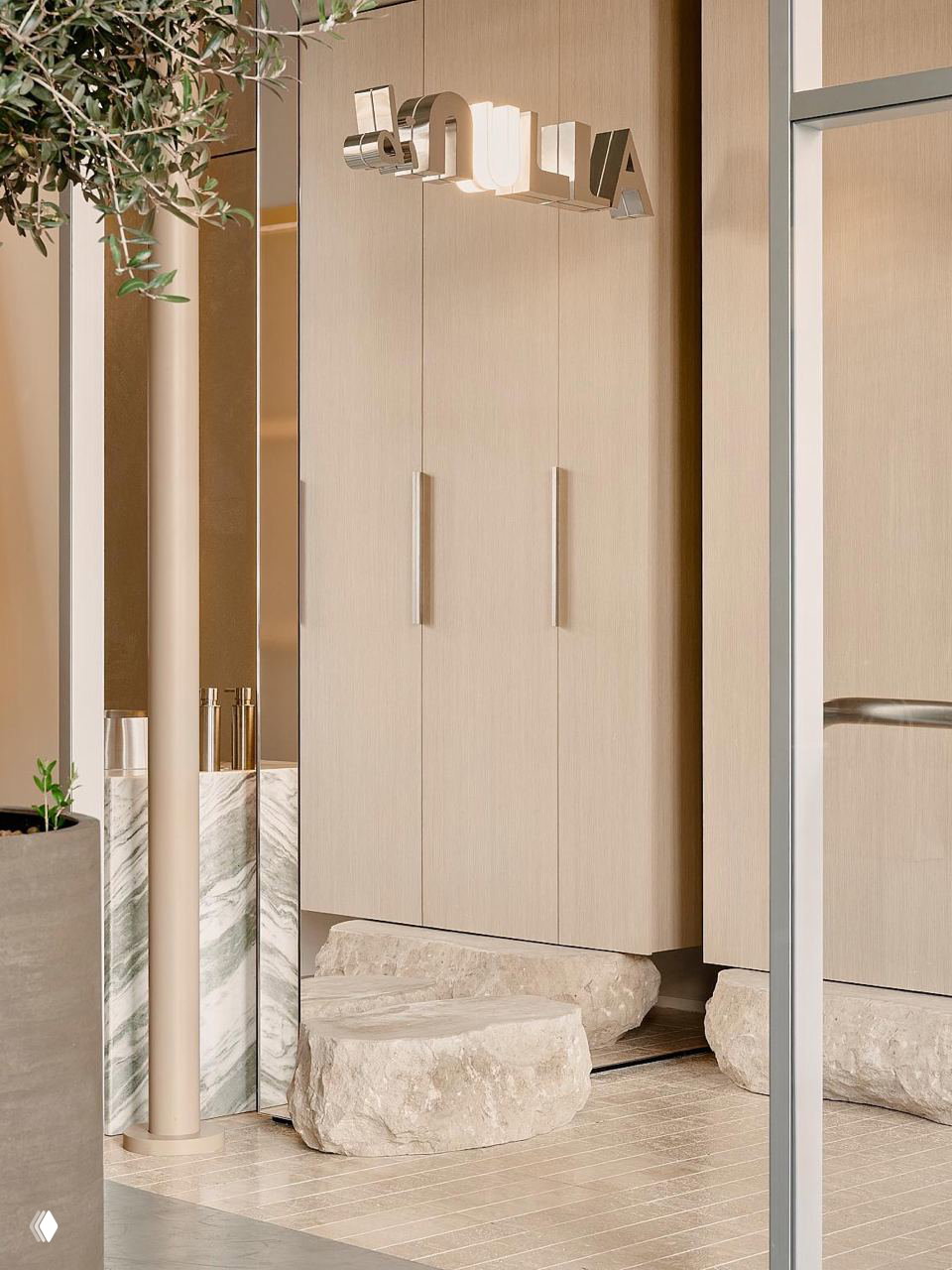 Деталь у входа: светлые встроенные шкафы, зеркальная вывеска Di Nulla и каменные скамьи — сочетание простоты и текстур в прихожей кафе.