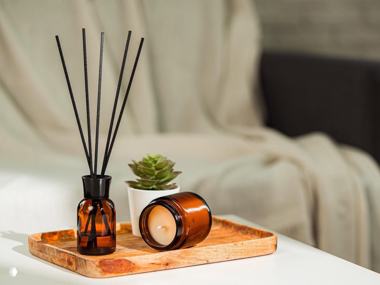 Янтарный стеклянный флакон‑диффузор и лежащая свеча на деревянном подносе рядом с небольшим суккулентом, уютная декоративная композиция в мягком свету студии.