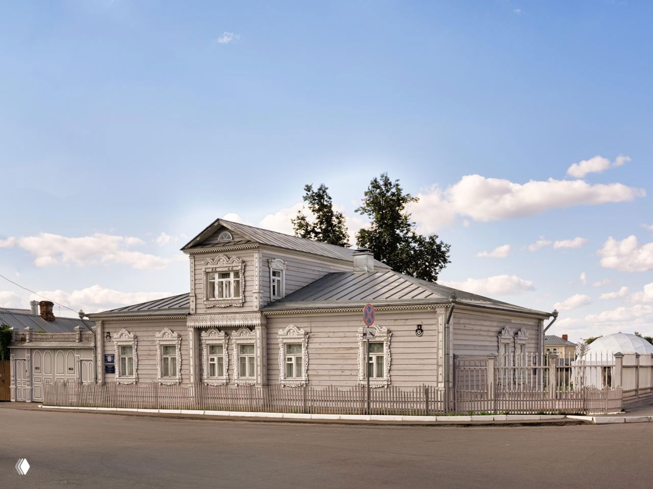 Традиционный деревянный купеческий дом в Коломне с резными наличниками, улица исторической застройки и спокойная городская сцена.