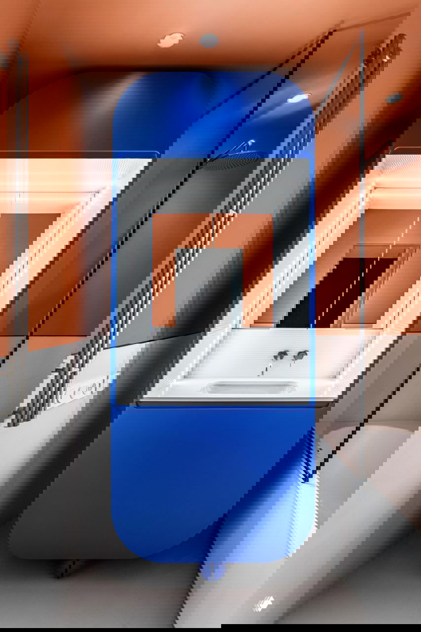 Ванная с ярко‑синим округлым умывальником-кабинетом на фоне тёплого терракотового тона стен и стеклянной душевой перегородки.