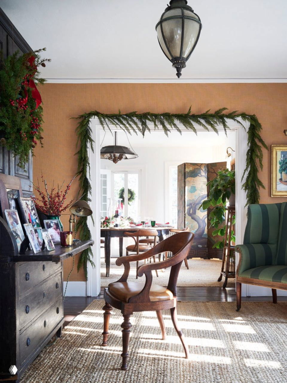 Интерьер с дверным проёмом, обрамлённым зелёными гирляндами, винтажной мебелью и естественным дневным освещением — тёплый праздничный антураж.