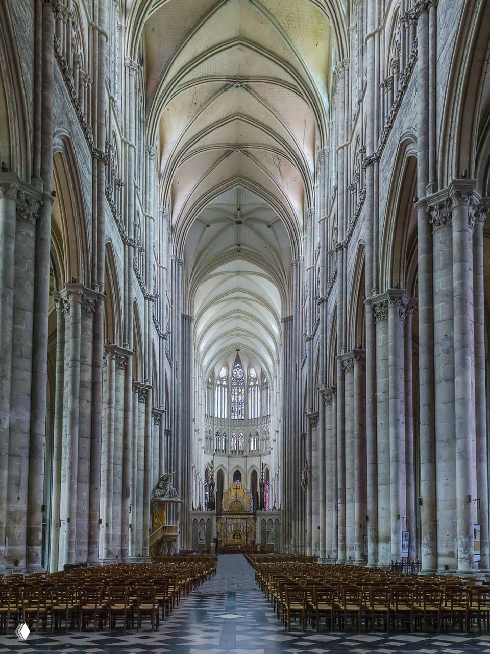 Высокий готический неф с ребристыми сводами и стройными колоннами, перспективный вид вдоль центральной оси к алтарю и витражам.