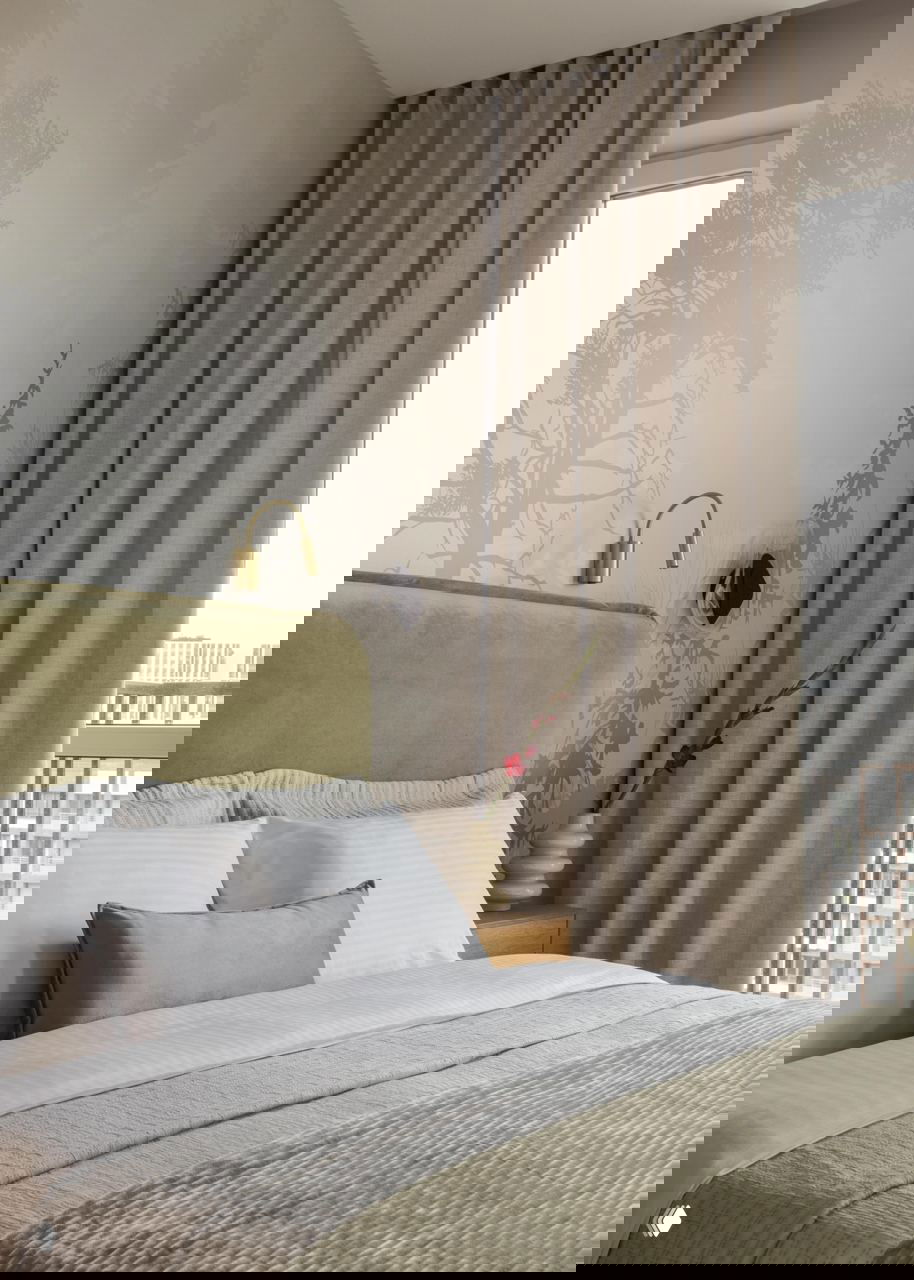 Спальная зона с бархатным зелёным изголовьем, аккуратной постелью и приглушёнными текстурами; лёгкие шторы и декоративный принт на стене.