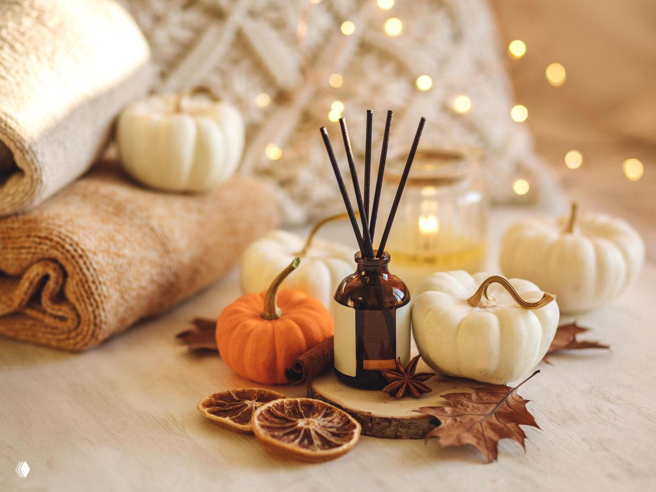 Коричневый стеклянный флакон с палочками среди осенних декоративных тыкв, сушёных долек цитруса и текстиля — тёплая сезонная композиция для уюта в студийном свете.