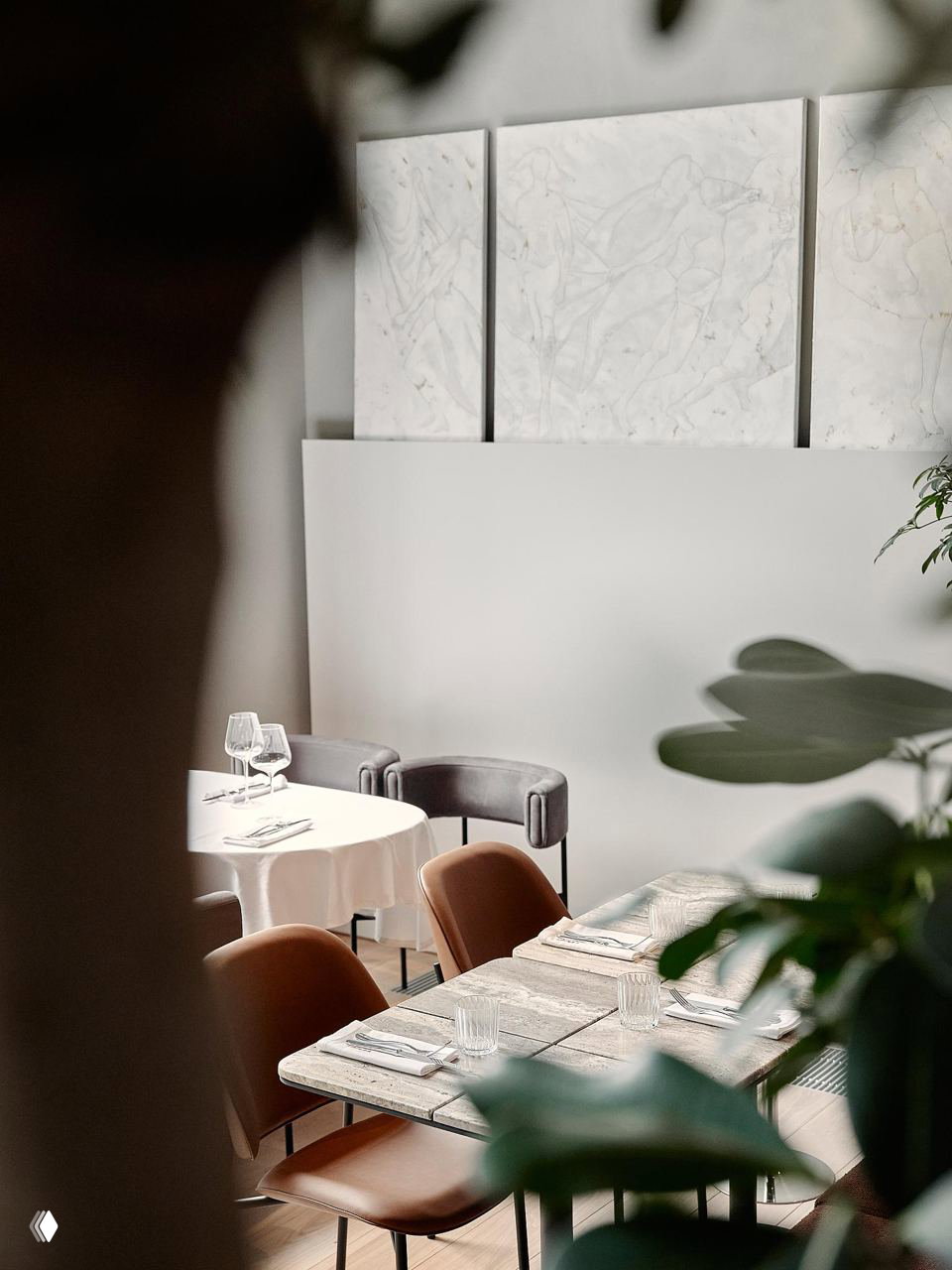 Вид через зелёные листья на столы с мраморными плитами и мягкими креслами, акцент на естественные материалы и «контролируемый хаос» в планировке.